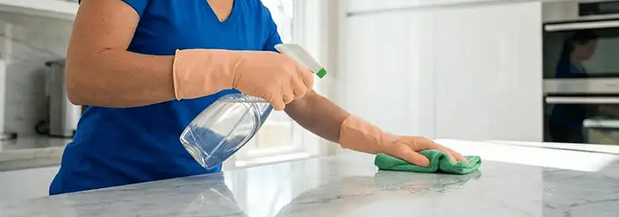 Maid service worker spraying and wiping a kitchen countertop with a microfiber cloth for sanitizing, Naperville, IL.