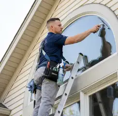 Professional window cleaner on a ladder using a squeegee to clean an exterior arched window, Naperville, IL.