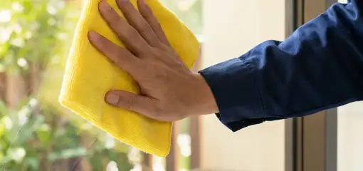 House cleaner wiping a glass window with a yellow microfiber cloth for streak-free cleaning, Naperville, IL.